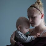 woman carrying baby with pacifier in mouth